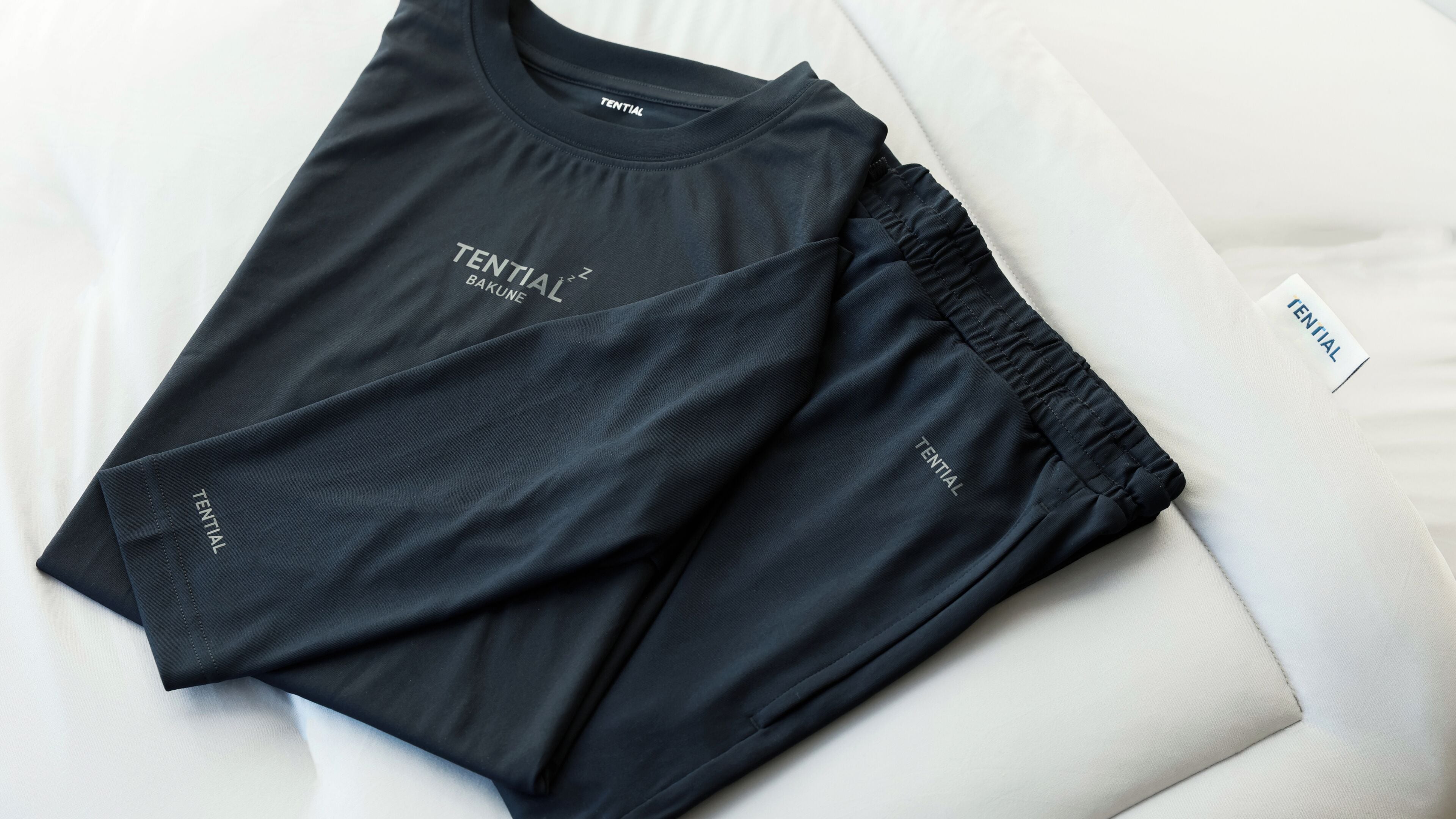 A black TENTIAL branded athletic outfit laid out on a white bed.