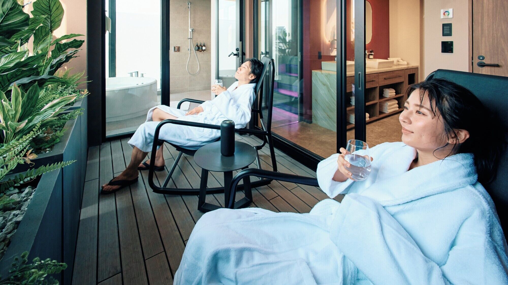 Ein moderner Spa-Bereich mit einer großen Badewanne, einer gläsernen Duschkabine und einer Sitzecke mit Blick auf die Stadt.