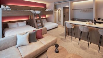 A modern, compact hotel room with a bunk bed, a sofa, a small bar area, and a mirror.