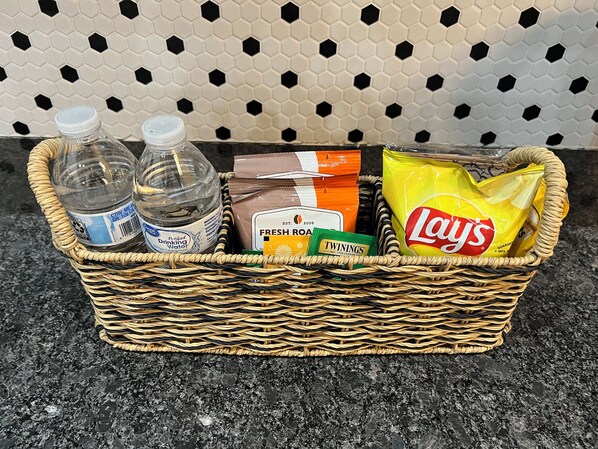 A wicker basket containing bottled water, fresh rooibos tea, Twinings tea, and Lay's potato chips.