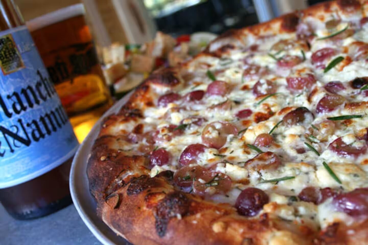 A pizza with visible toppings and a beverage in the background.