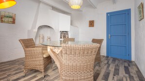 Un comedor con sillas de mimbre, una mesa de cristal, una puerta azul y una pared blanca con chimenea.
