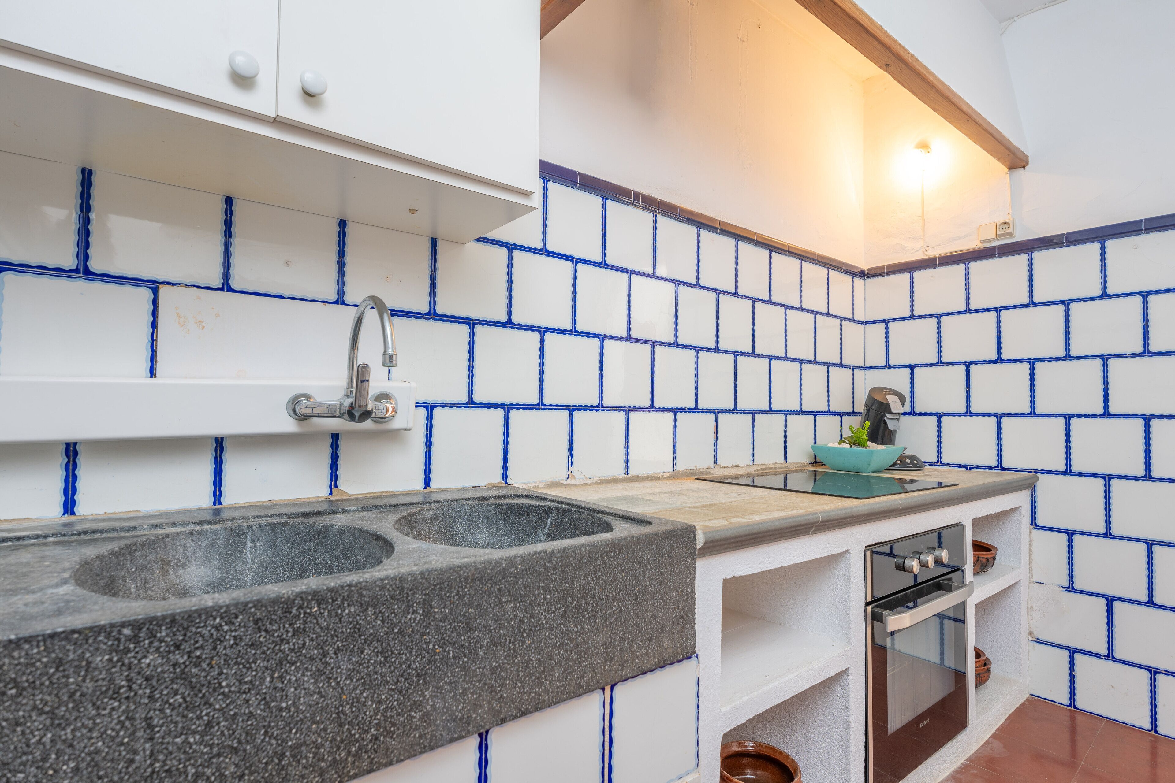 Cocina con armarios blancos, encimera de granito, lavamanos doble, estufa y paredes con azulejos azules.