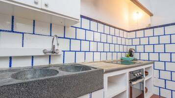Cocina con armarios blancos, encimera de granito, lavamanos doble, estufa y paredes con azulejos azules.