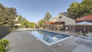 Una piscina con un deck circundante, mobiliario exterior y un edificio de techo rojo.