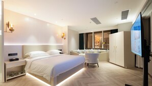 Ett modernt hotellrum med en stor säng, sängbord, en sittgrupp med en fåtölj, en TV och en garderob.