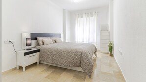 A bedroom with a bed, nightstand, lamp, and a window with curtains. - RentitSpain Varadero: Beach, Sea, and Comfort (Motril)