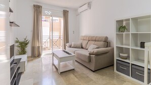 A modern living room with a sofa, a coffee table, a TV, and a balcony with curtains. - RentitSpain Varadero: Beach, Sea, and Comfort (Motril)