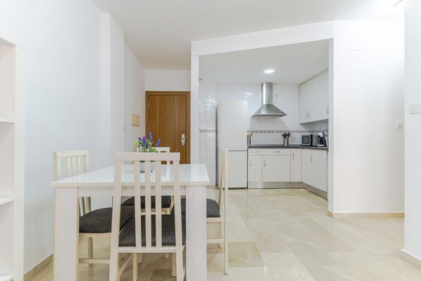 Cozy living area with a dining table for two, a vase with flowers, and a fully equipped kitchen in the background.
