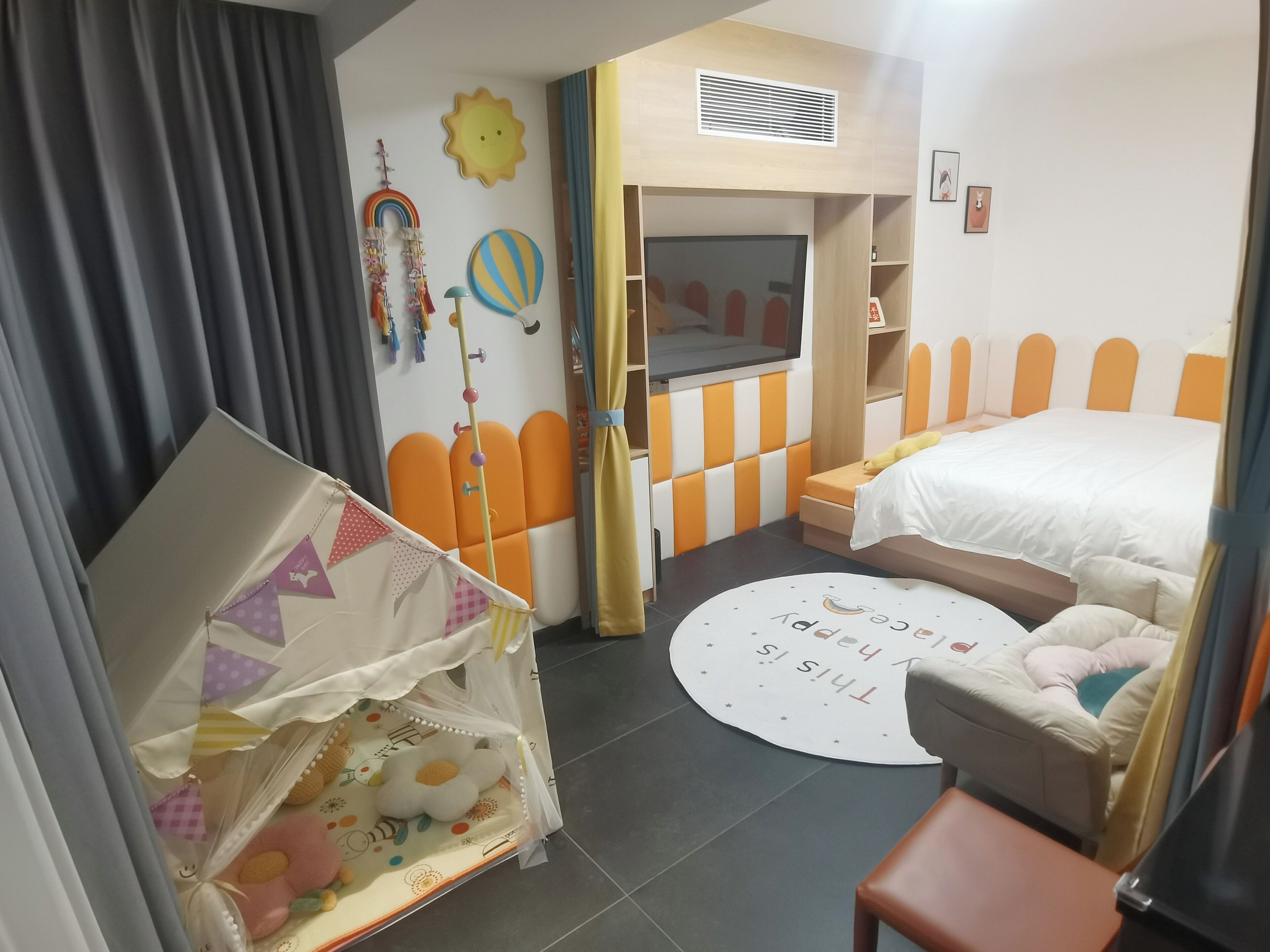 Een kinderkamer met een bed, een speelhoek en een rond vloerkleed met tekst.