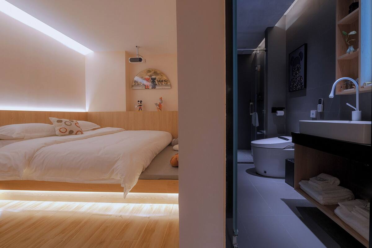 Ein modernes Schlafzimmer mit einem großen Bett, einem Holzkopfende und einem an der Decke befestigten Projektor.