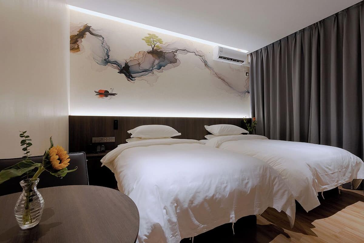 Ein Hotelzimmer mit einem großen Bett, einem Nachttisch, einer Vase mit Blumen und einem Wandbild.