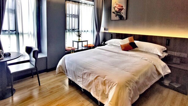 Camera d'albergo moderna con un letto grande, una scrivania e una sedia. Si vede una finestra con tende, una pianta in vaso e un quadro appeso al muro.
