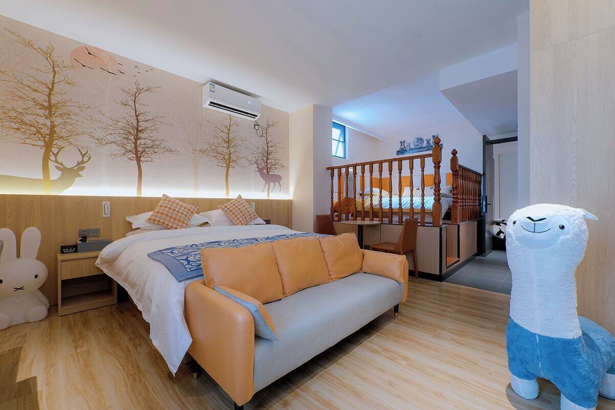 Ein Schlafzimmer mit Bett, Sofa, Nachttisch, Wand-Klimaanlage, einer Holztreppe und einem Stofftier.