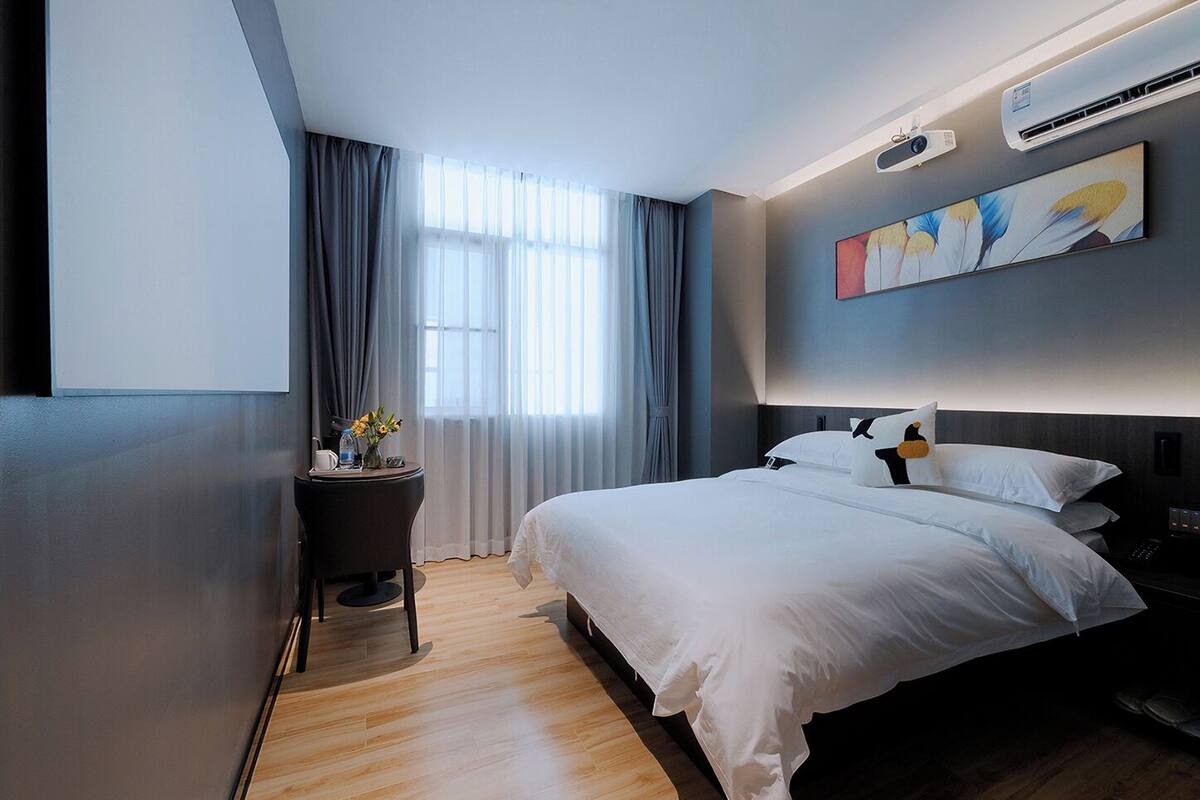 Ein modernes Hotelzimmer mit einem großen Bett, einem Schreibtisch mit Lampe und einem Gemälde an der Wand.