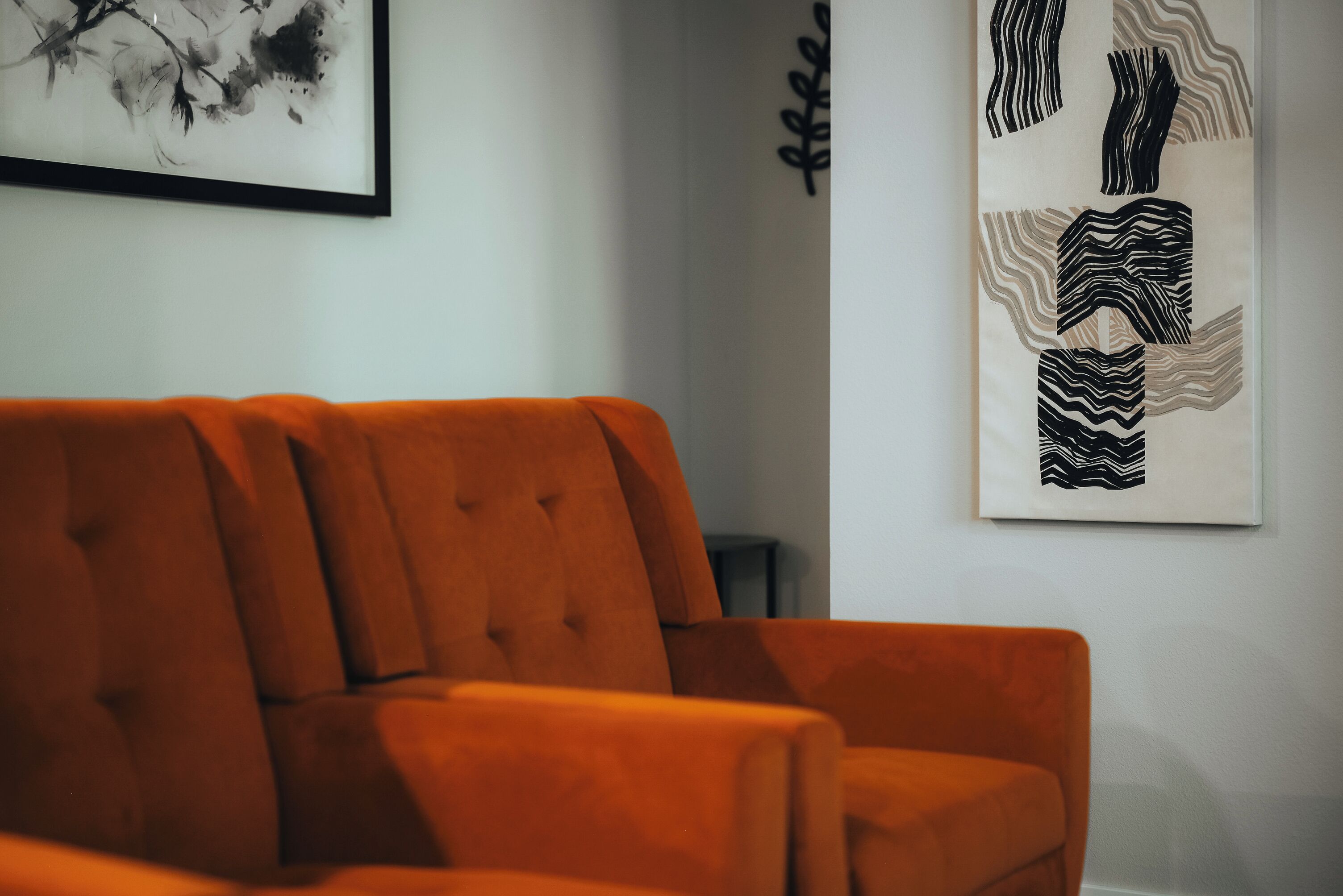 Un salon moderne avec un canapé orange à motifs capitonnés, un tableau abstrait encadré et une œuvre d’art murale à texture intéressante.