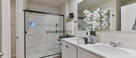 A modern bathroom with a glass-enclosed shower, a large mirror, and a white sink.