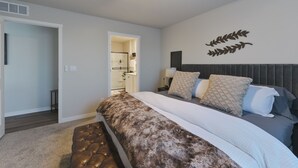 A bedroom with a bed, a ceiling fan, a wall-mounted light, and a door leading to a bathroom.