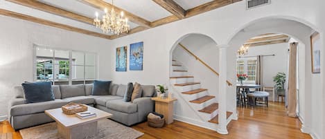 A spacious living room with a gray sectional sofa, wooden flooring, and a staircase leading to another room.