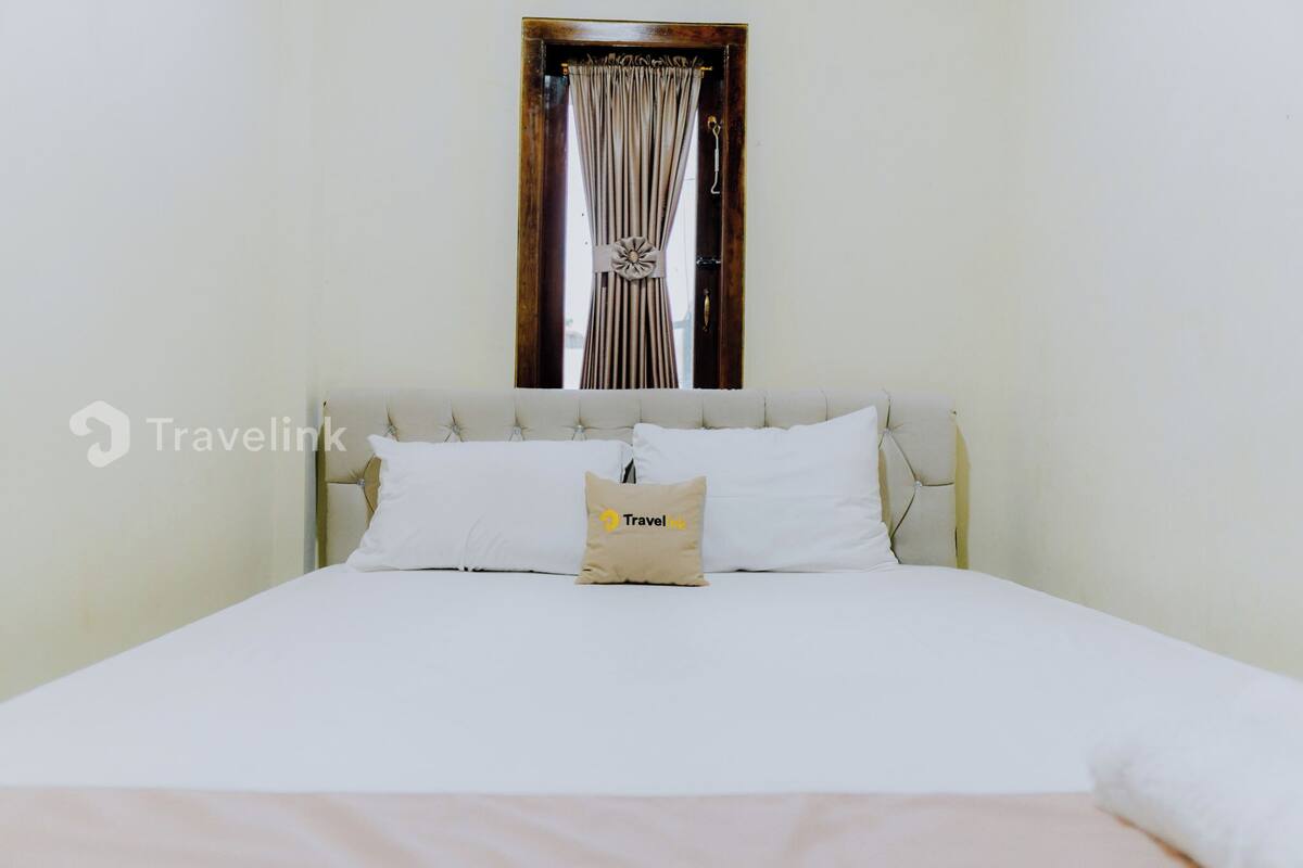 Un lit bien fait, avec du linge de lit blanc et un seul oreiller beige orné d’un logo de marque de voyage.