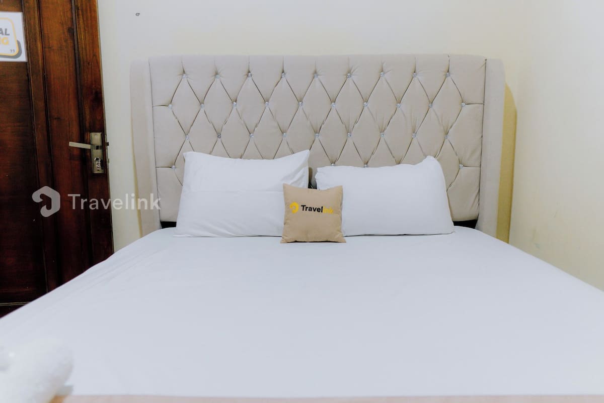 Un lit avec une tête de lit capitonnée, deux oreillers blancs et un oreiller marron orné d’un logo.