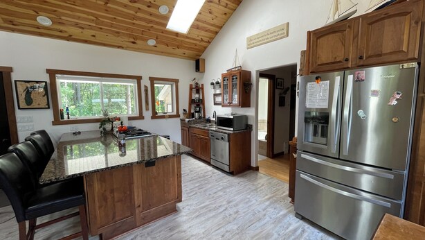 Une cuisine moderne avec des meubles en bois, un réfrigérateur en acier inoxydable, un grand îlot central et une vue sur l’extérieur.