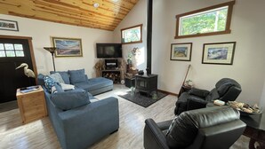 Un salon chaleureux avec un canapé bleu, un fauteuil en cuir noir, un plafond en bois et une cheminée.