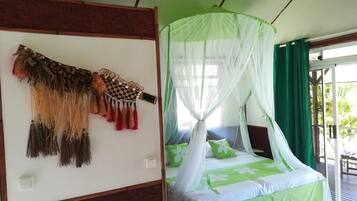 A room with a bed under a canopy, a wall with a decorative hanging, and a view of the outdoors.