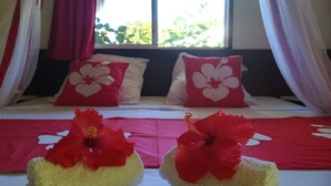 Een hotelkamer met een bed, twee rode kussens met witte bloemmotieven en een rode en witte spreideken.