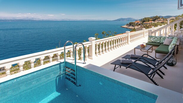 A pool with a view of the sea, a white balustrade, and a seating area with a table and chairs. - Villa Linda (Blato)
