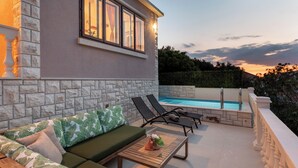 A patio with a pool, a green sofa, and lounge chairs. - Villa Linda (Blato)