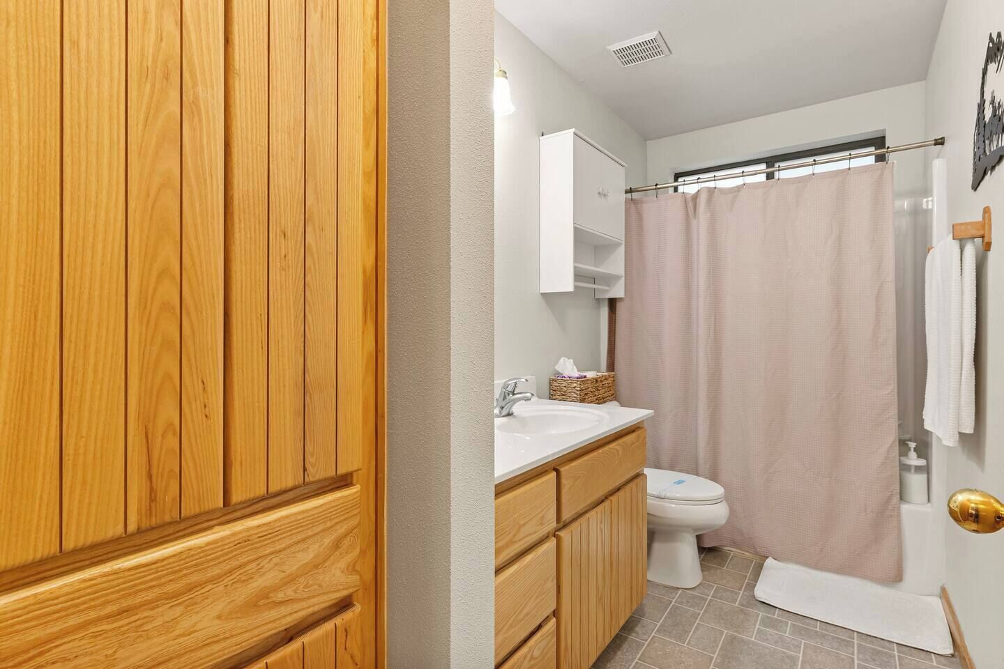 A bathroom with a wooden vanity, a white sink, a toilet, and a shower curtain.