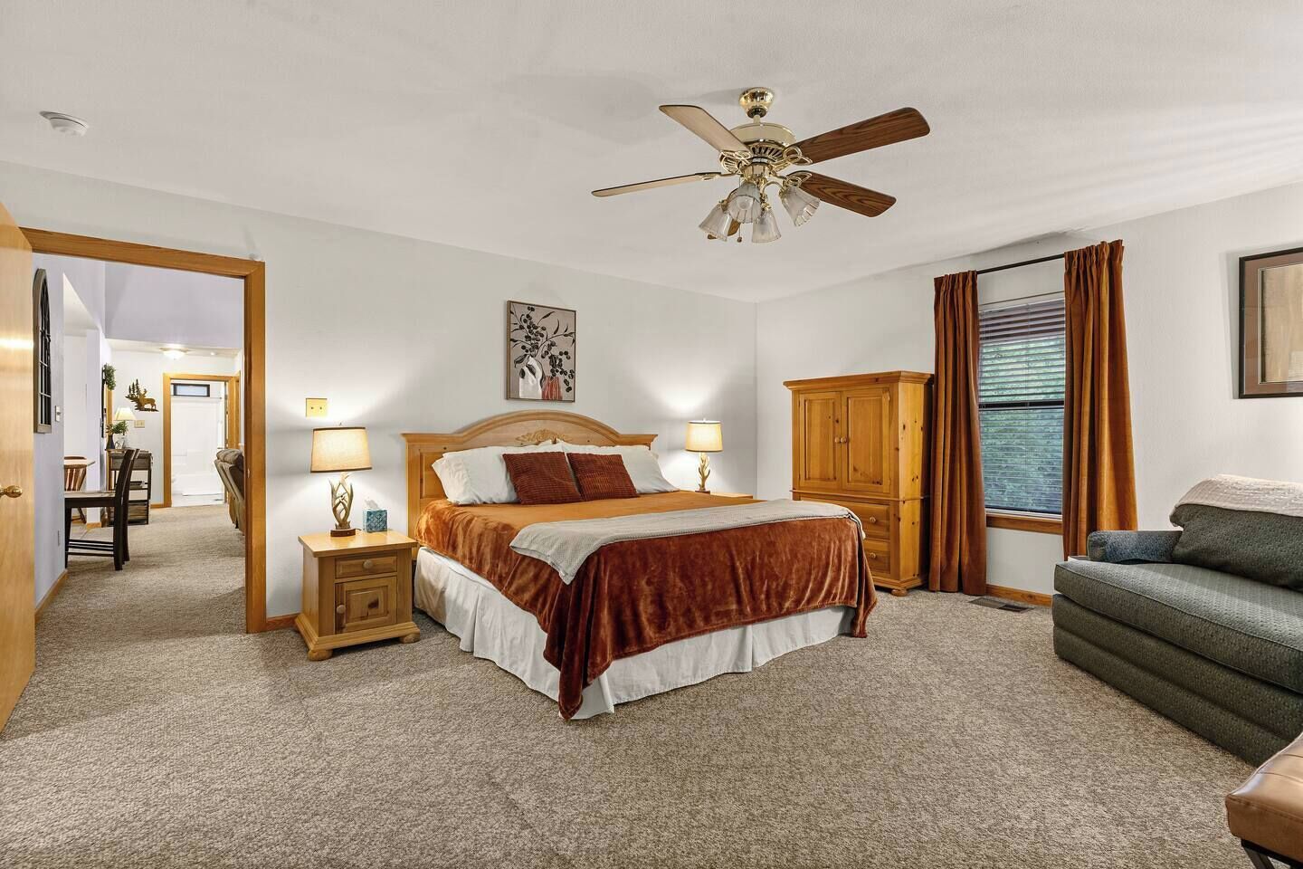 A hotel room with a bed, bedside tables, a ceiling fan, a wardrobe, a sofa, and a window with curtains.