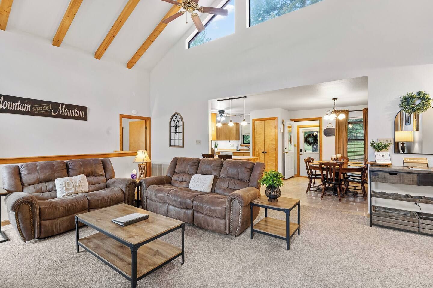 A spacious living room with a large brown leather sofa, a coffee table, and a dining area with wooden furniture.