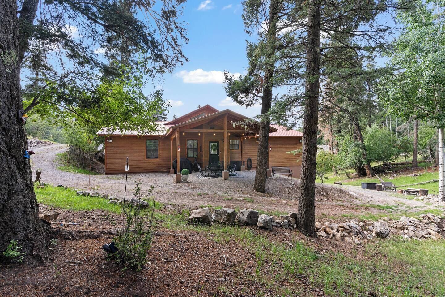 A wooden cabin with a porch, surrounded by trees and a gravel driveway.