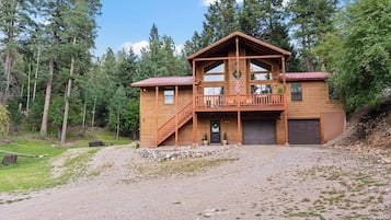 A two-story wooden cabin with a balcony, a front porch, and a garage.