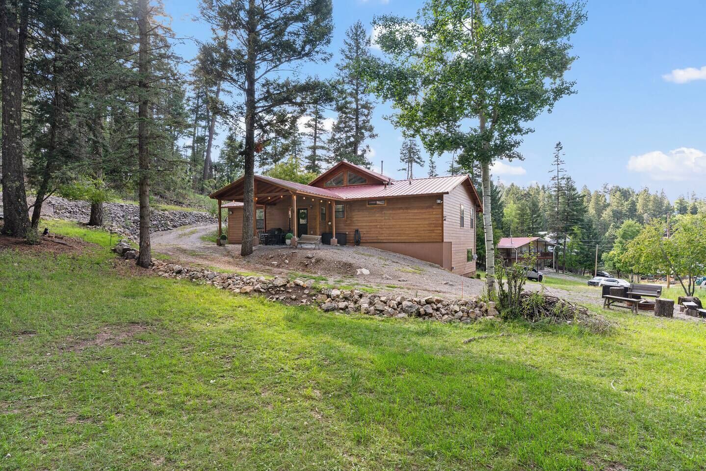 A cabin with a porch, surrounded by a stone wall, and a grassy area with trees.