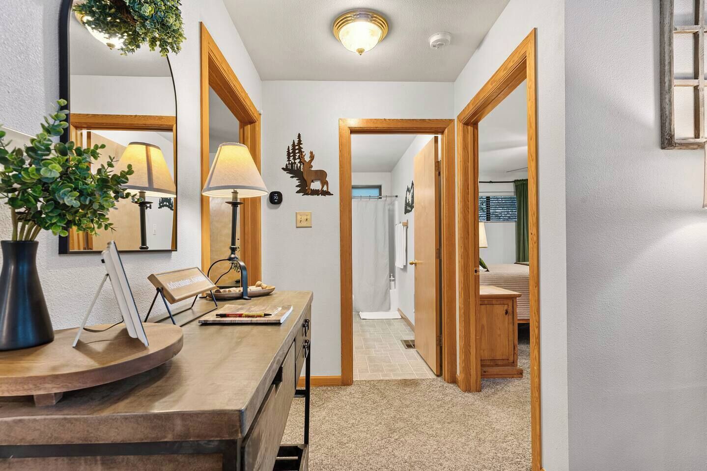 A hallway with a desk, lamp, and a plant. There are wooden doors leading to other rooms.