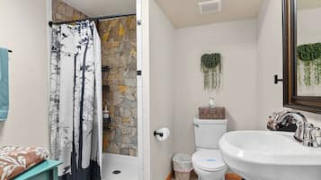 A bathroom with a shower, toilet, sink, and a stone wall.