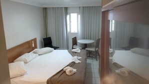 Una habitación de hotel con una cama, una silla, una mesita y un ventanal con cortinas.