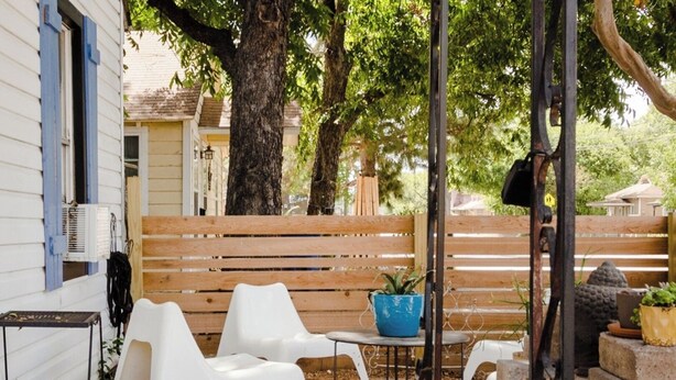 Eine Terrasse mit weißen Kunststoffstühlen, einem kleinen runden Tisch und einem blauen Blumentopf.