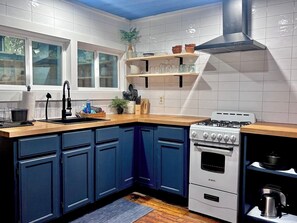 A kitchen with white tiled walls, blue cabinets, a gas stove, and a sink with a modern faucet.