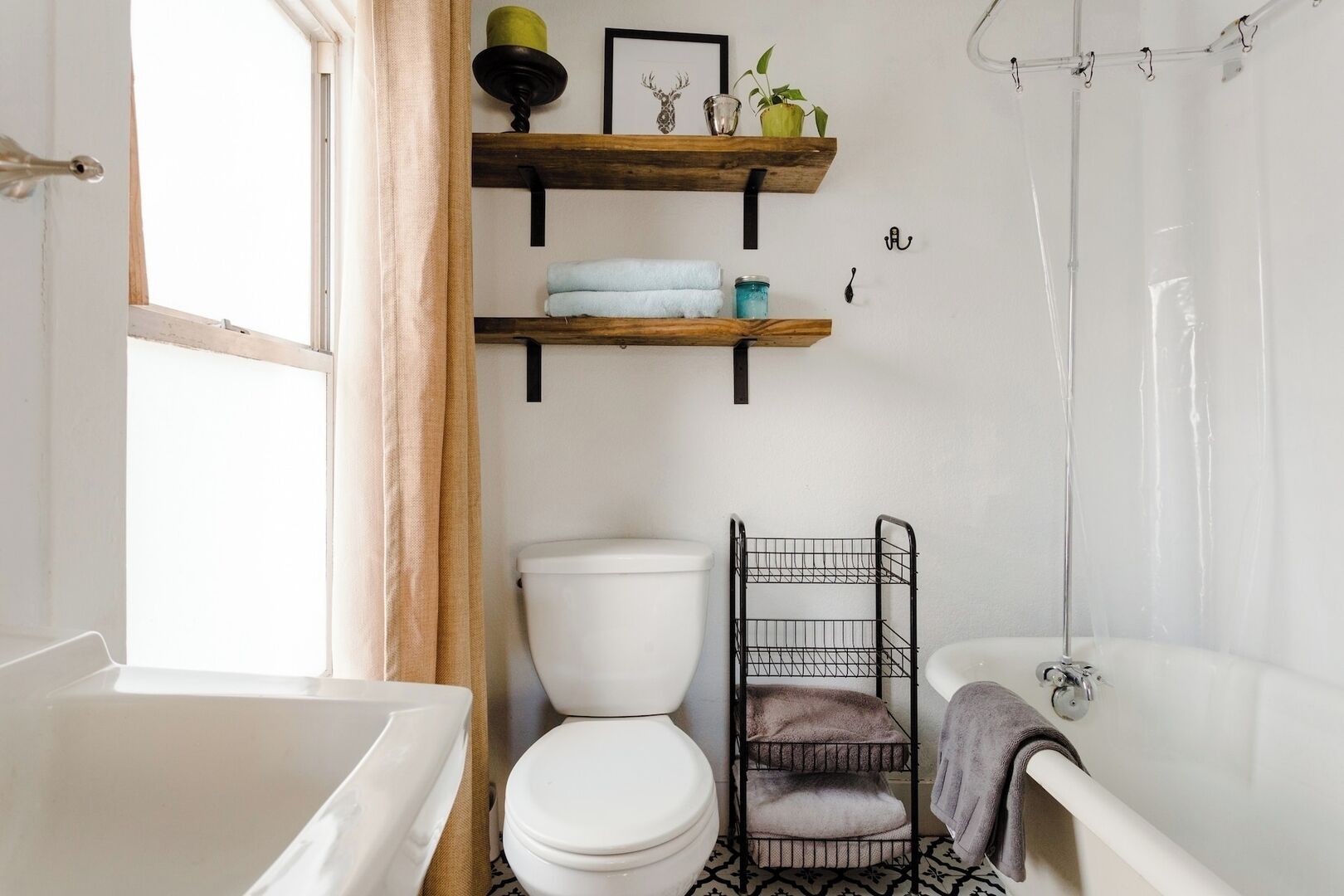 A bathroom with a white bathtub, a white toilet, a shower, and a black metal shelf with towels.