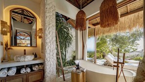 A bathroom with a stone wall, a large mirror, a bathtub, and a view of the outdoors. - Munay Wasi Uluwatu (Pecatu)
