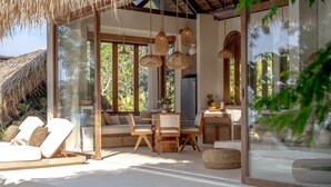 A modern, open-plan living area with a glass wall, wooden furniture, and hanging wicker lights. - Munay Wasi Uluwatu (Pecatu)