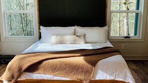 Un dormitorio con una cama grande, dos ventanas y vista a árboles.