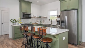 Una cocina con armarios verdes, un refrigerador de acero inoxidable, un microondas y una isla grande con taburetes de bar.