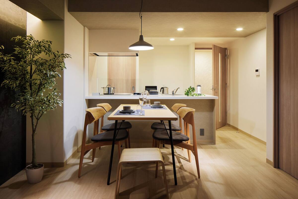 A modern kitchen with a dining area, wooden flooring, and a potted plant.