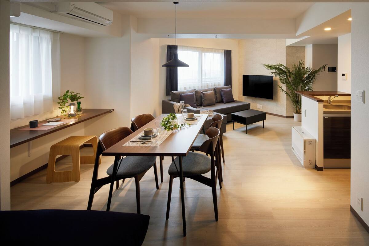 A modern living room with a dining area, a sofa, a TV, and a kitchen area.