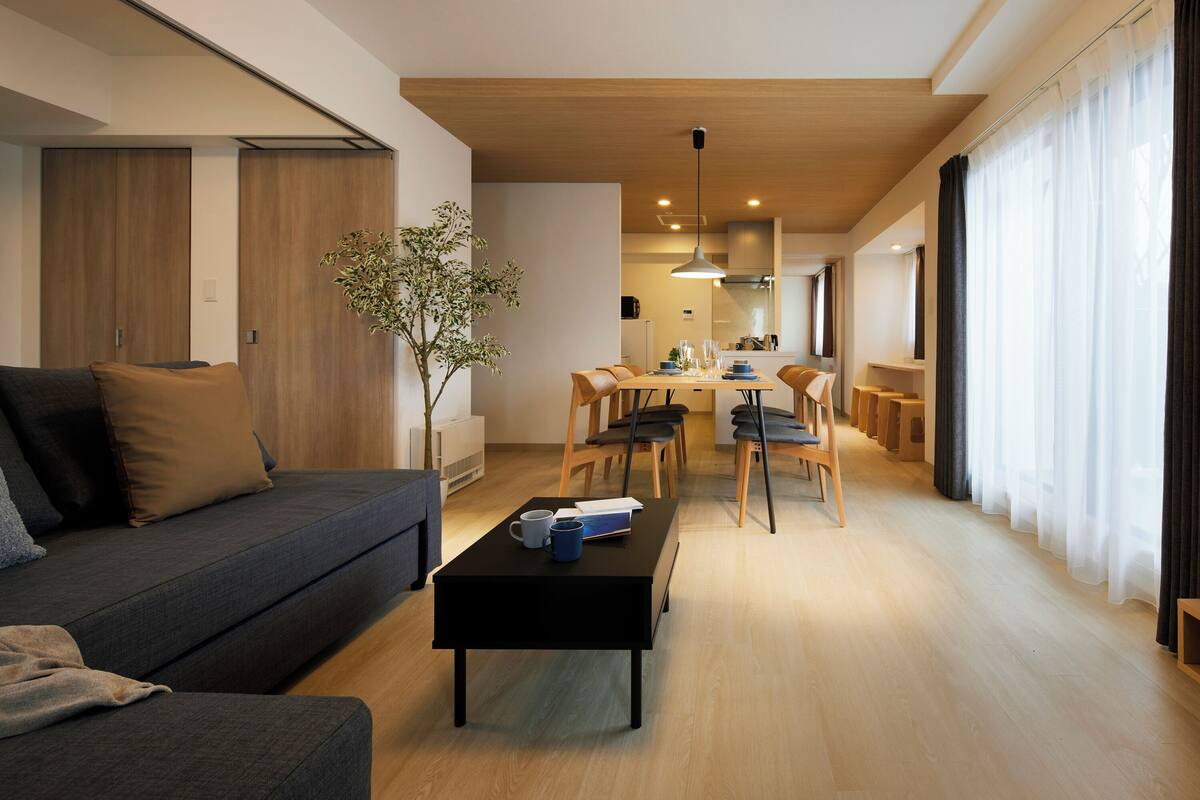 A modern living room with a sofa, coffee table, dining area, and a plant.